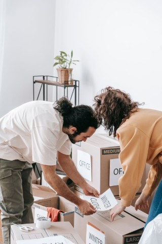 Two friends packing moving boxes and labelling them Office, Closet and Winter.
